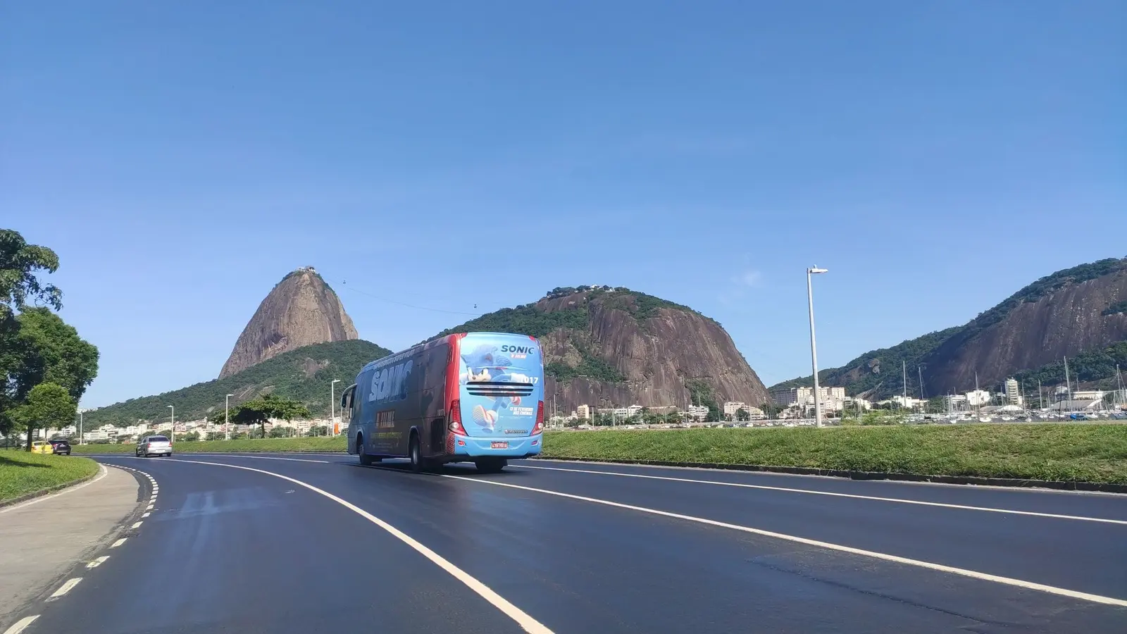 Ônibus envelopado passando pelo Aterro do Flamengo com o Pão de Açúcar ao fundo